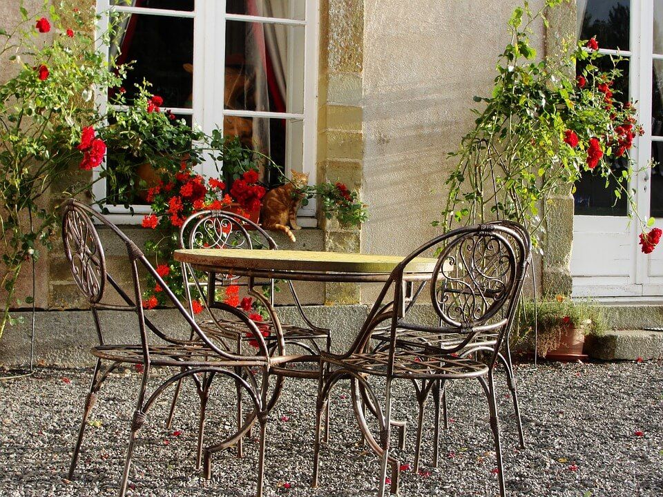 Wrought iron chairs sit around a patio table next to a building.