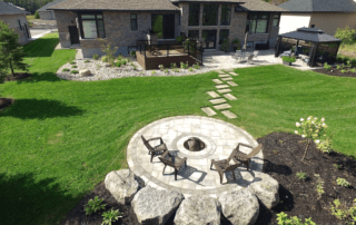 aerial view of low-maintenance backyard landscaping with firepit and interlocking stone