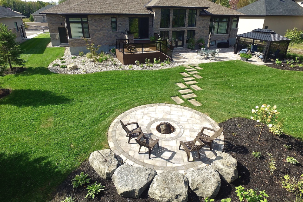 aerial view of low-maintenance backyard landscaping with firepit and interlocking stone